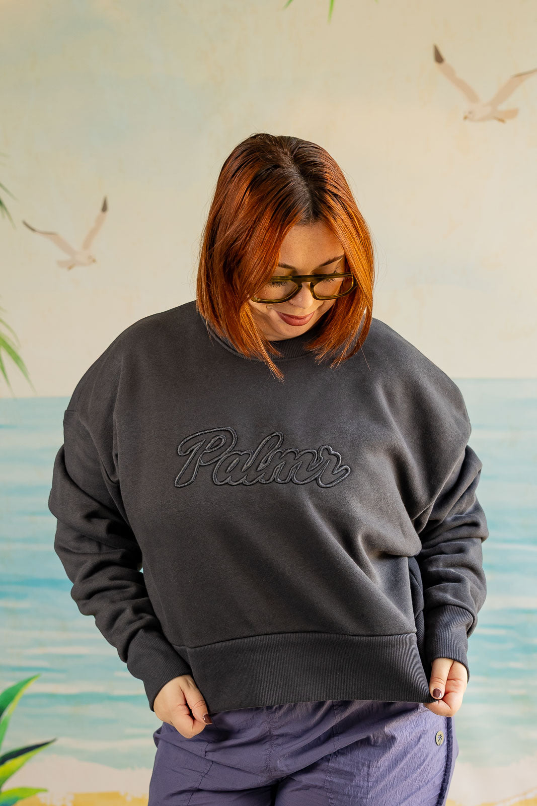 Person wearing a dark gray sweatshirt with 'Palmer' logo against a beach-themed wall.