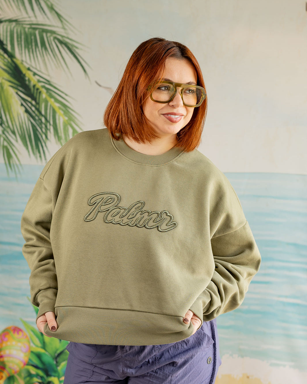 Person wearing a green sweatshirt with 'Palmer' text against a tropical-themed background
