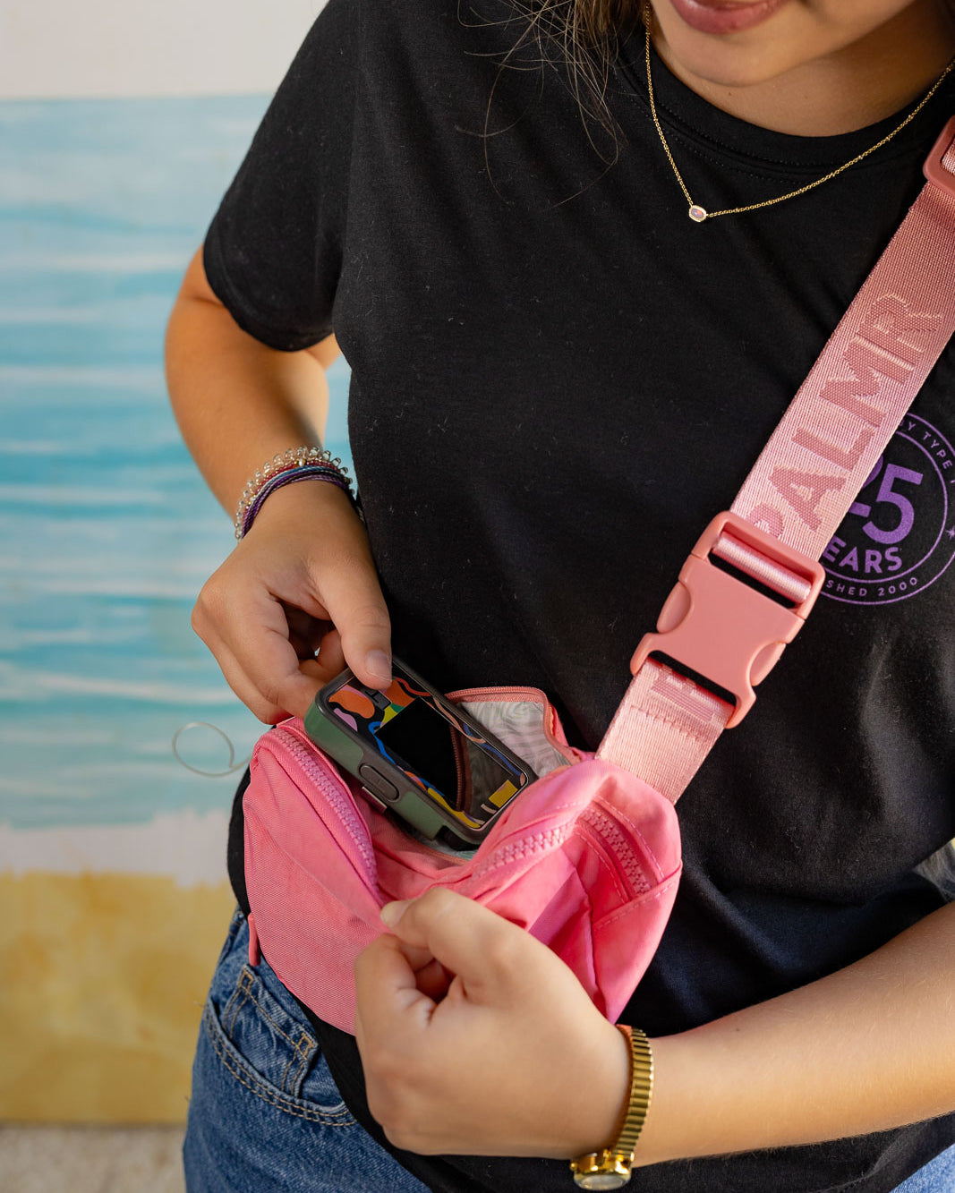 Person wearing a black t-shirt with a palm tree design, holding a pink bag.