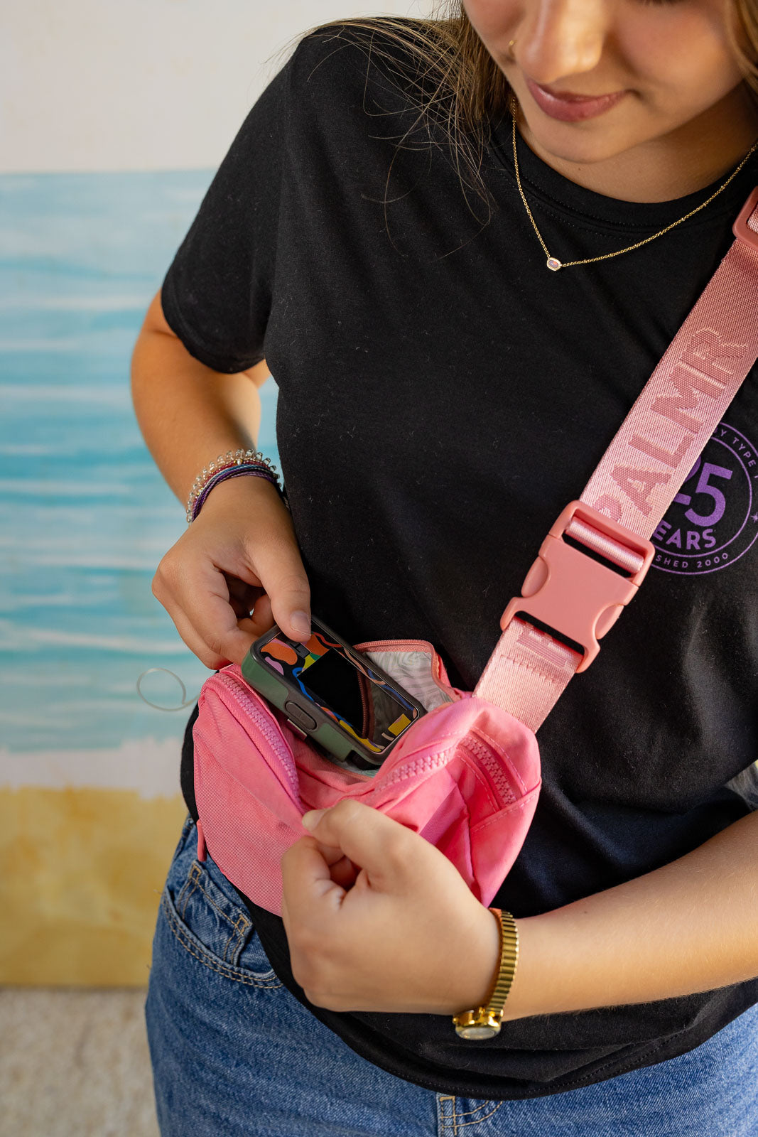 Person wearing a black t-shirt with a palm tree design, holding a pink bag.
