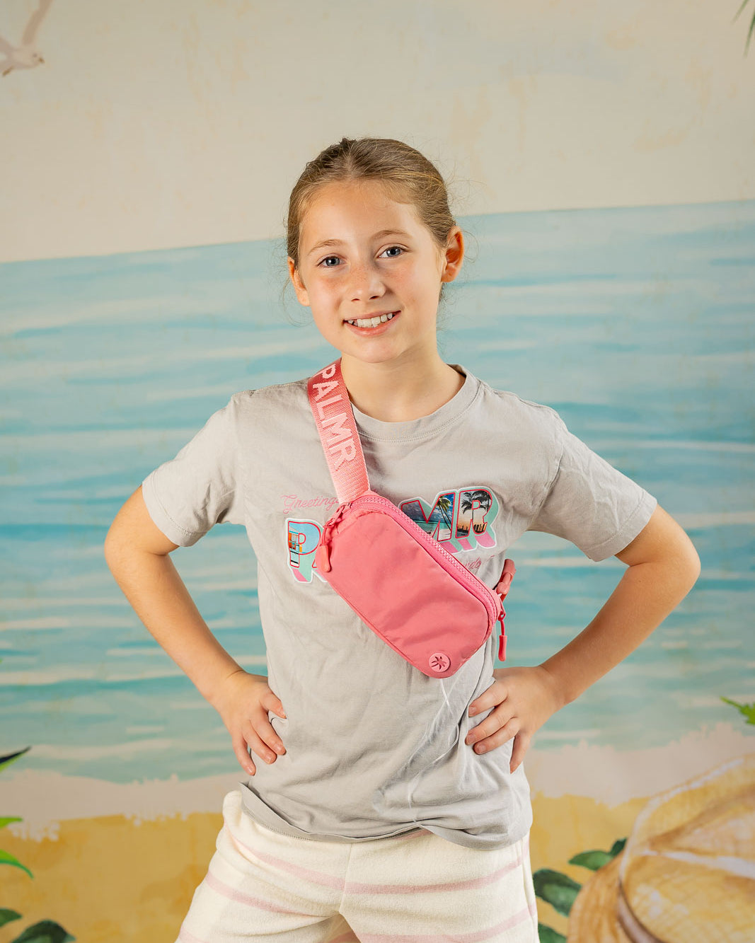 Young girl wearing a pink fanny pack with a beach-themed mural in the background