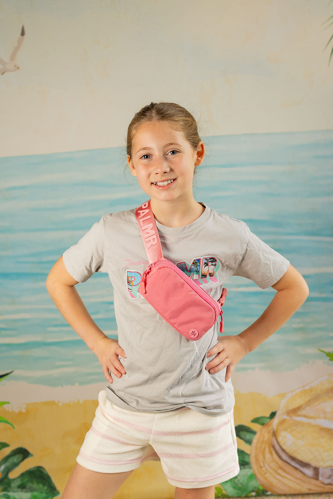 Young girl wearing a pink fanny pack with a beach-themed mural in the background