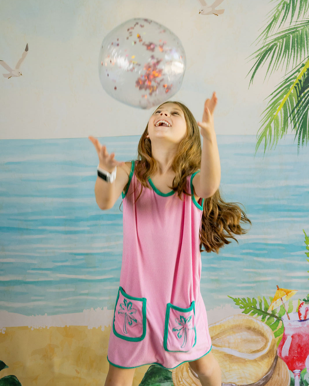 Young girl in a pink dress playing with a balloon against a beach-themed backdrop