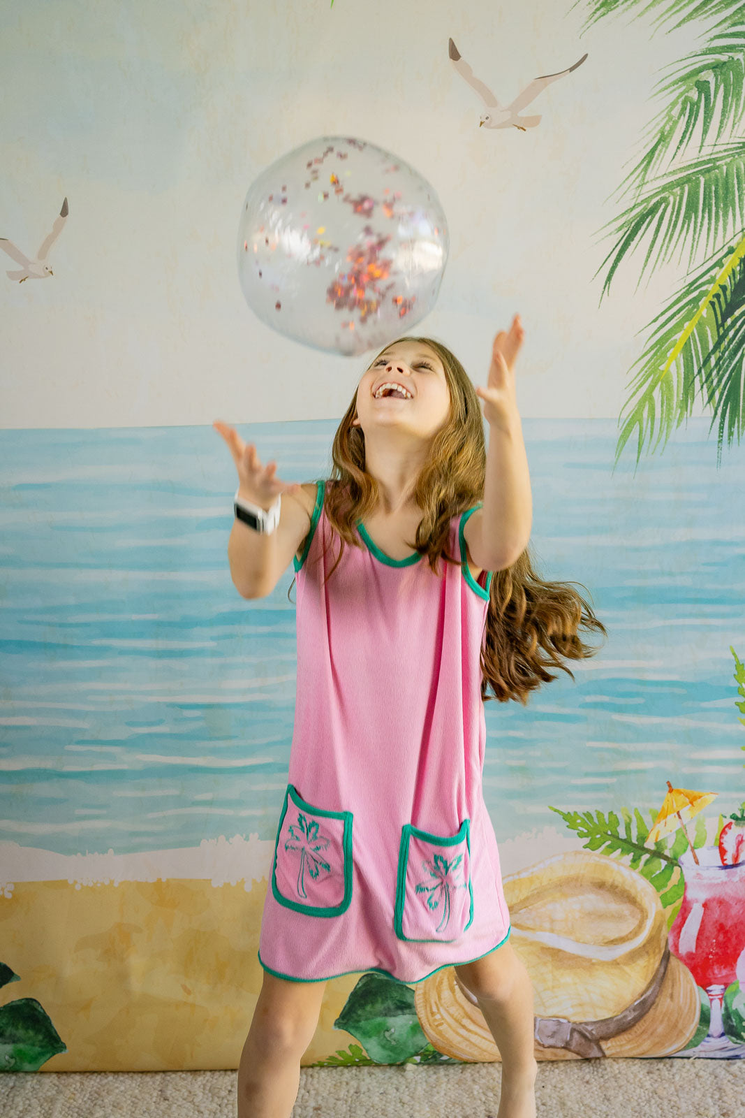 Young girl in a pink dress playing with a balloon against a beach-themed backdrop