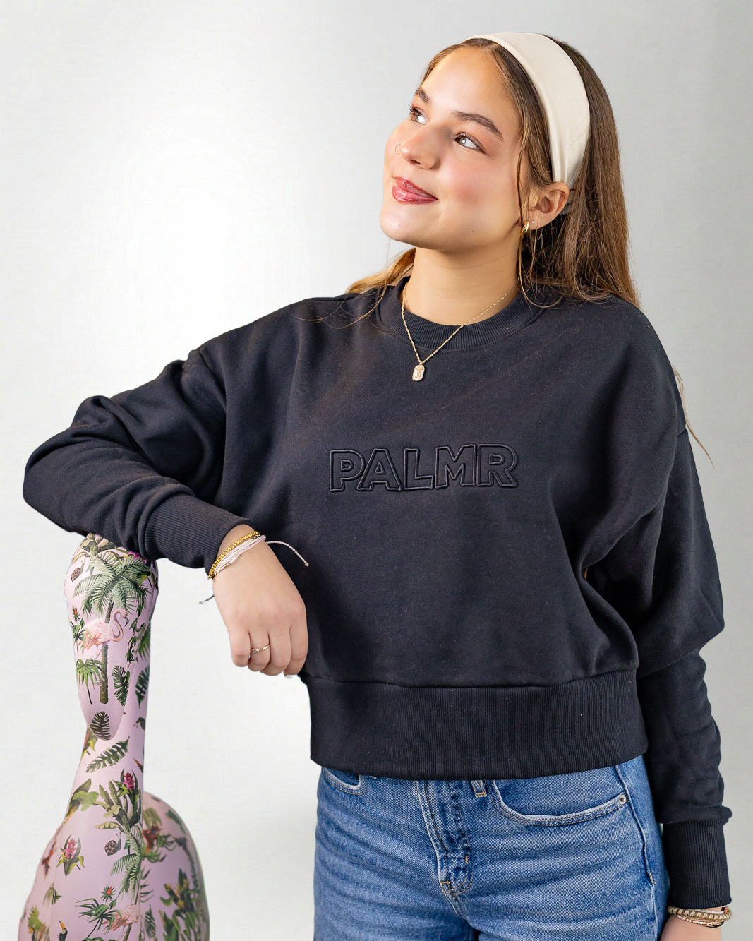 Woman wearing a navy blue sweatshirt with 'PALMR' branding, holding a floral-patterned bag against a white background.