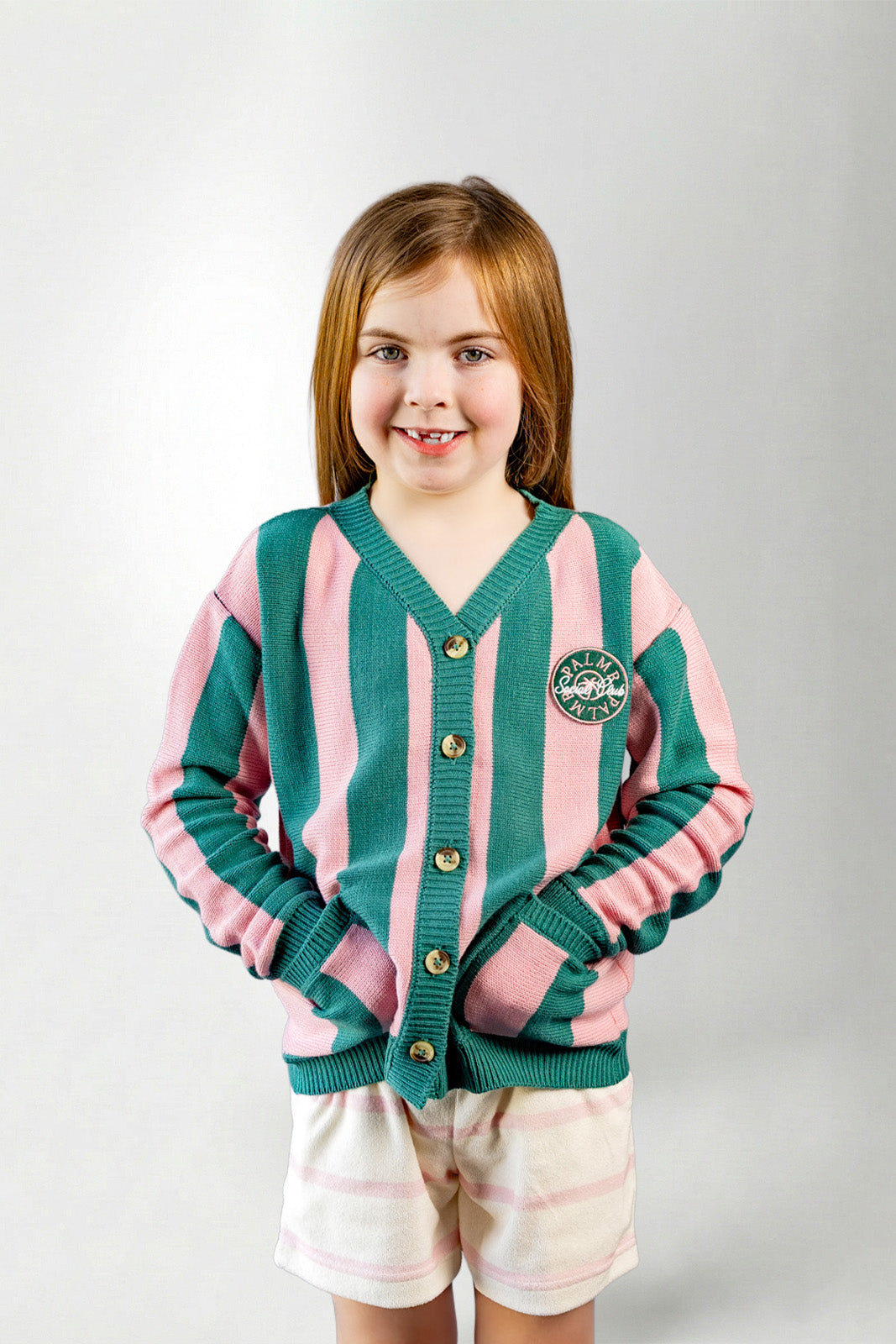 Young girl wearing a green and pink striped cardigan on a light gray background