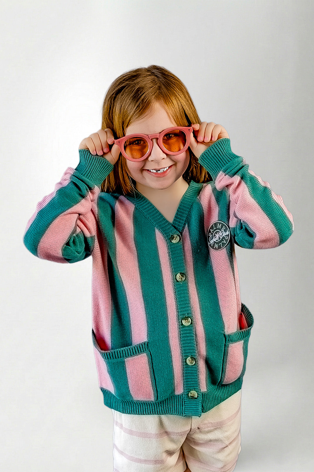 Child wearing a pink and green striped cardigan with sunglasses on a white background