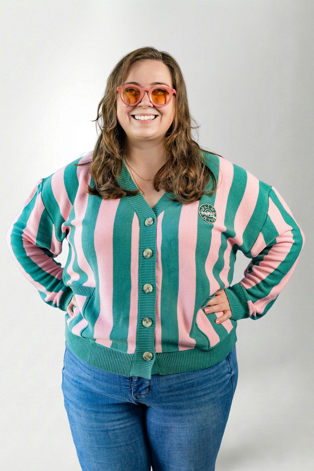 Person wearing a green and pink striped cardigan with a logo on a white background