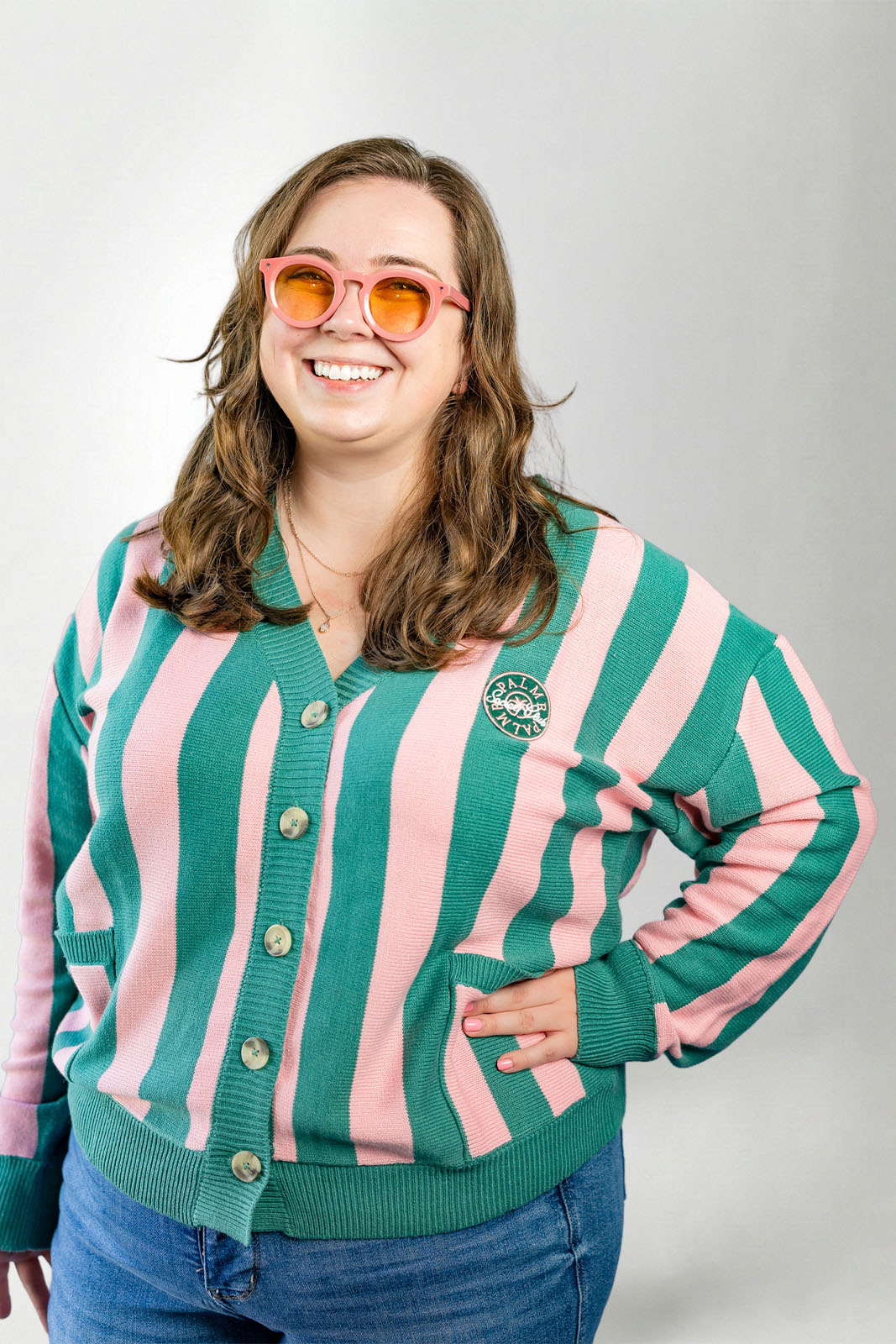 Person wearing a green and pink striped cardigan with a logo on a plain background