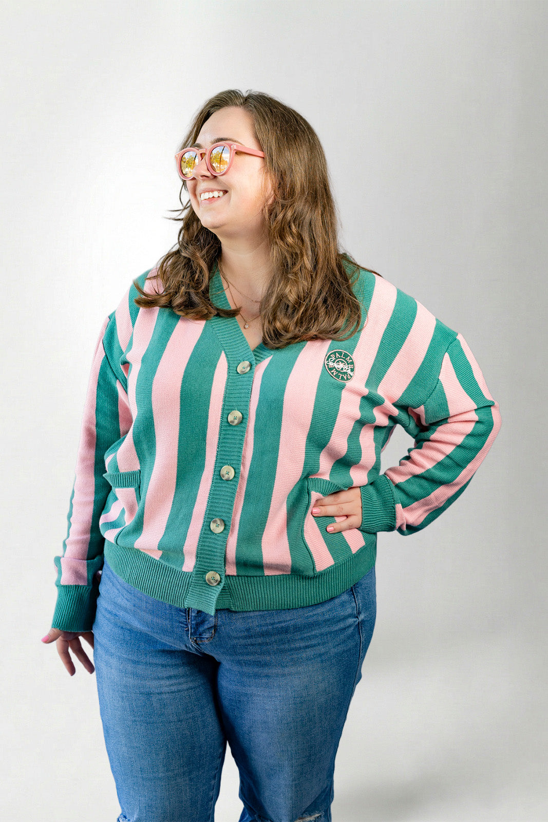 Person wearing a green and pink striped cardigan with a logo on a white background