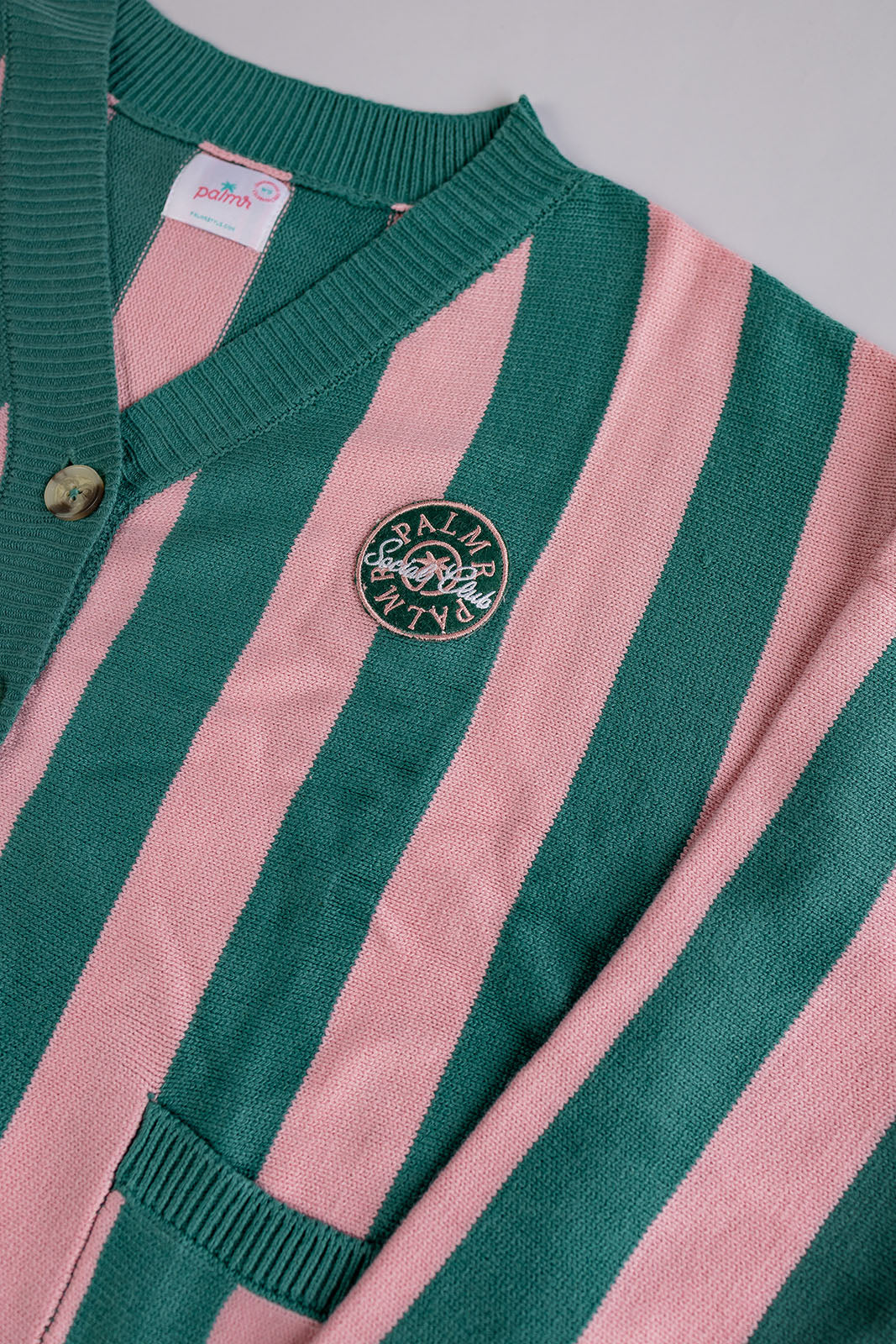 Green and pink striped cardigan with a brand logo on a gray background