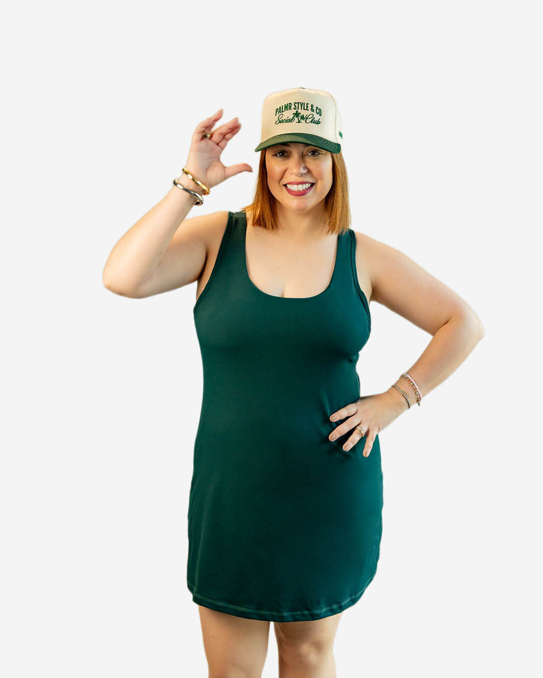 Woman wearing a green tank dress and a cap on a white background