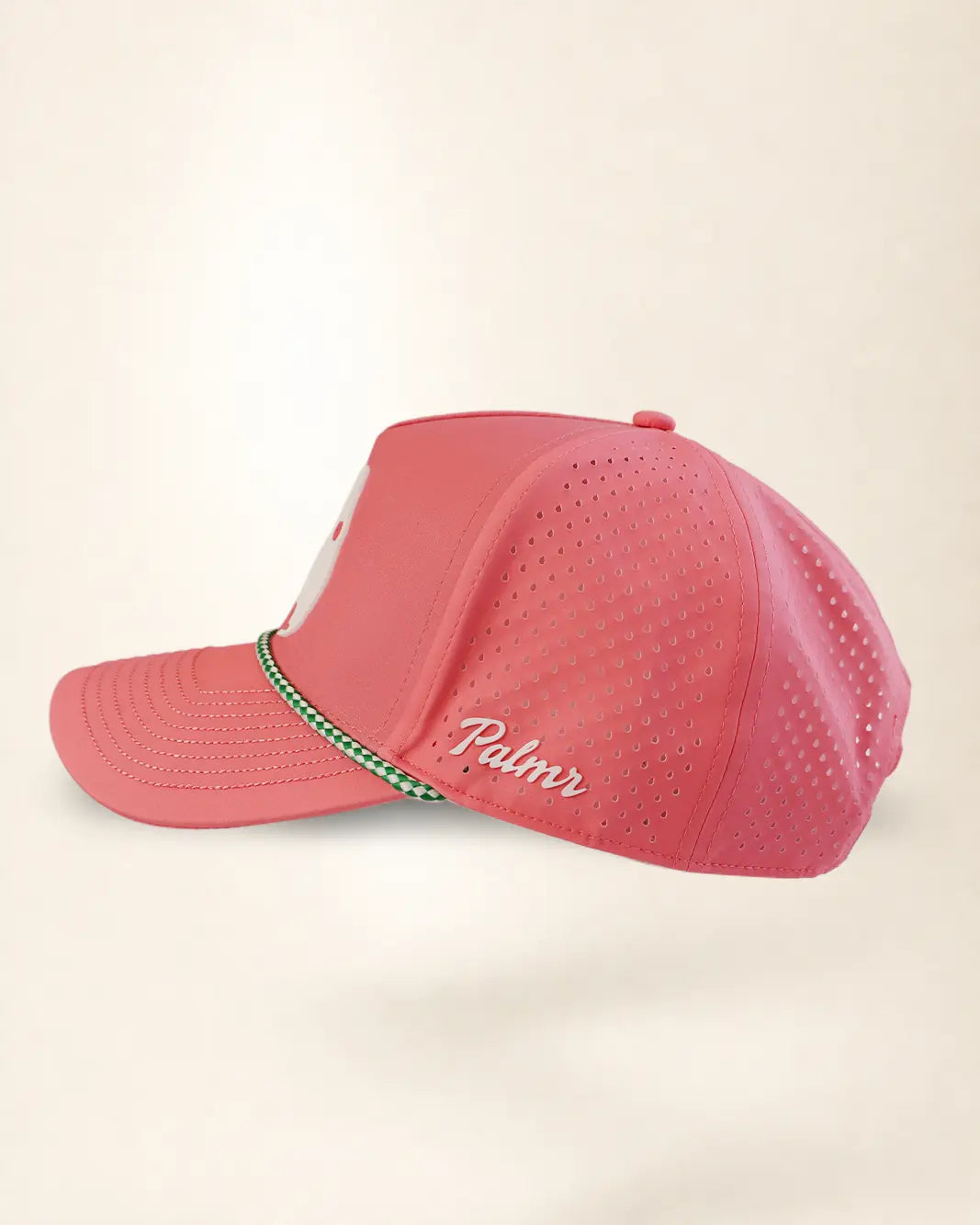 A pink perforated baseball cap with a green and white patterned trim along the brim and white 'Palmr' script embroidery on the side, shown against a light beige background.