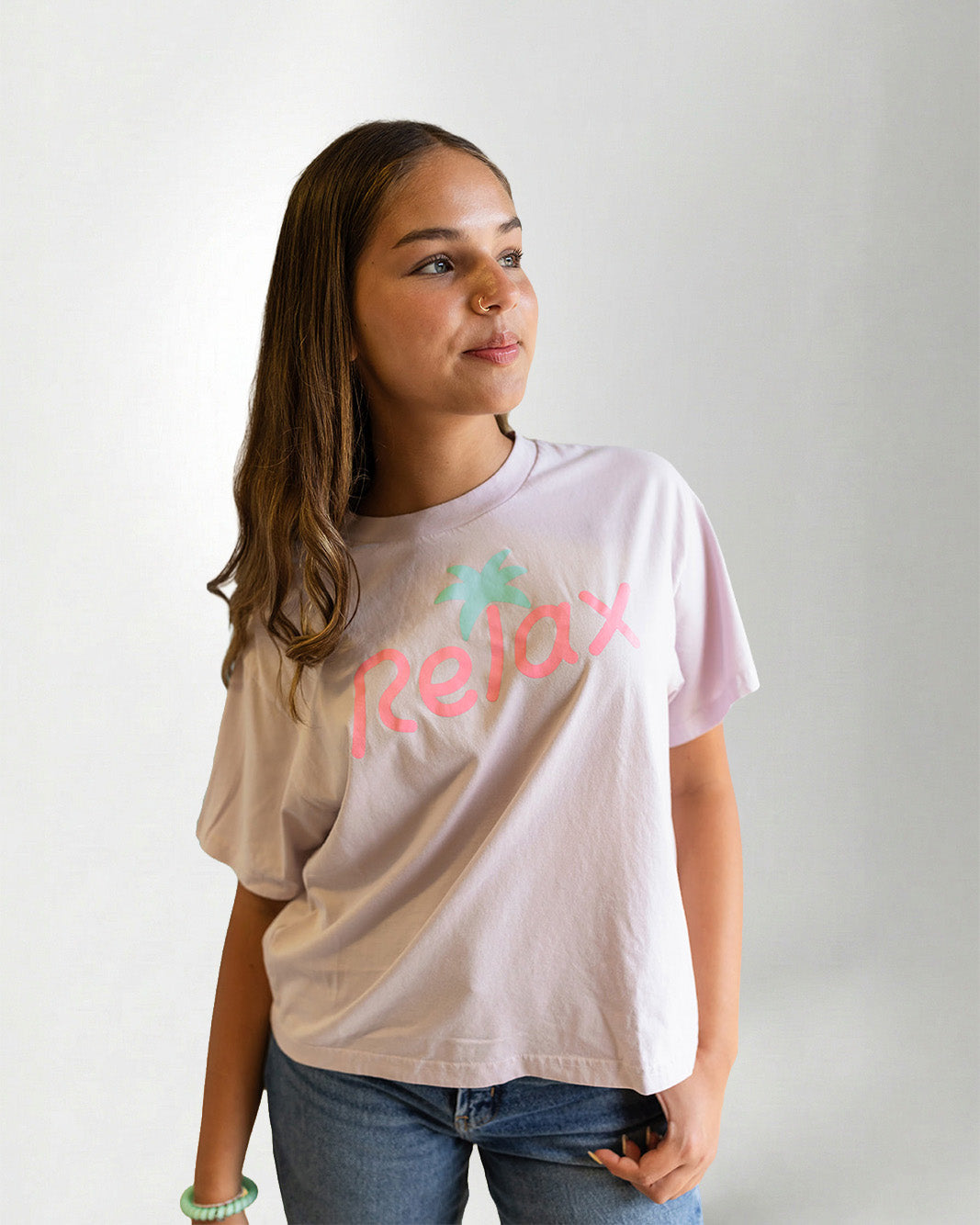Person wearing a light pink t-shirt with 'Relax' printed on it against a plain background
