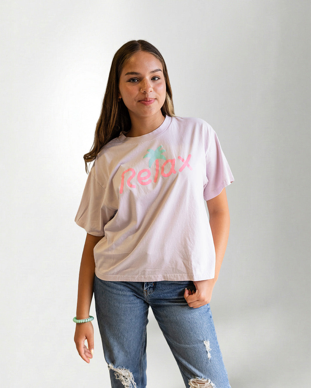 Person wearing a light pink t-shirt with 'Relax' printed on it against a plain background