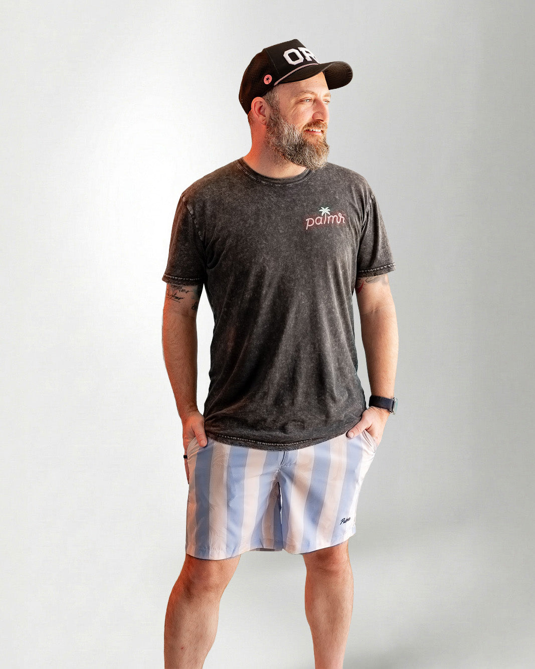 Man wearing Palmr Style Mens Ronnie Hybrid Swim Shorts Blue Tan Stripe Palm leaf Resort Wear and a black tee against a white background