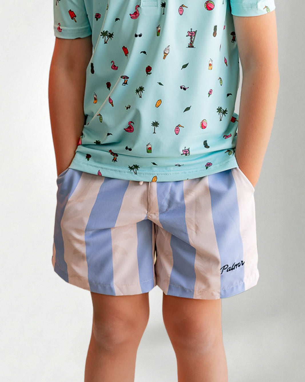 Person wearing a light blue patterned shirt and striped shorts on a plain background