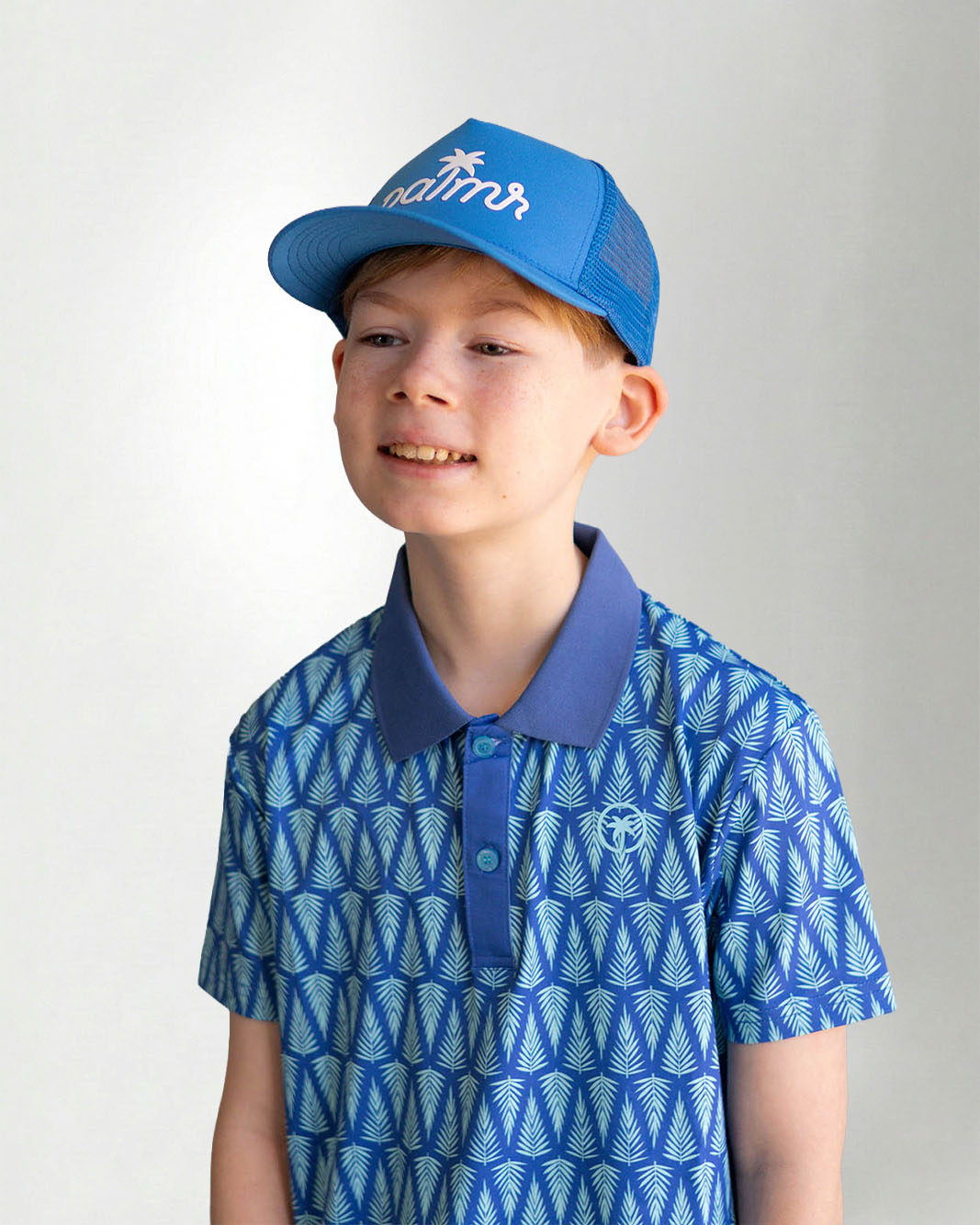 Child wearing a blue patterned polo shirt and cap with a white background