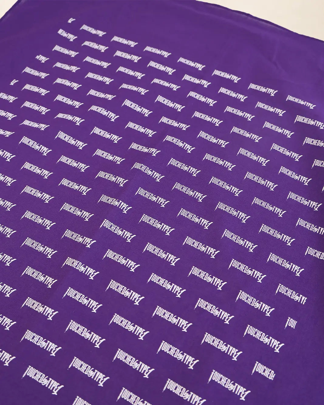 A close-up of a purple fabric surface printed repeatedly with the word 'Touched By Type 1' in white stylized lettering.