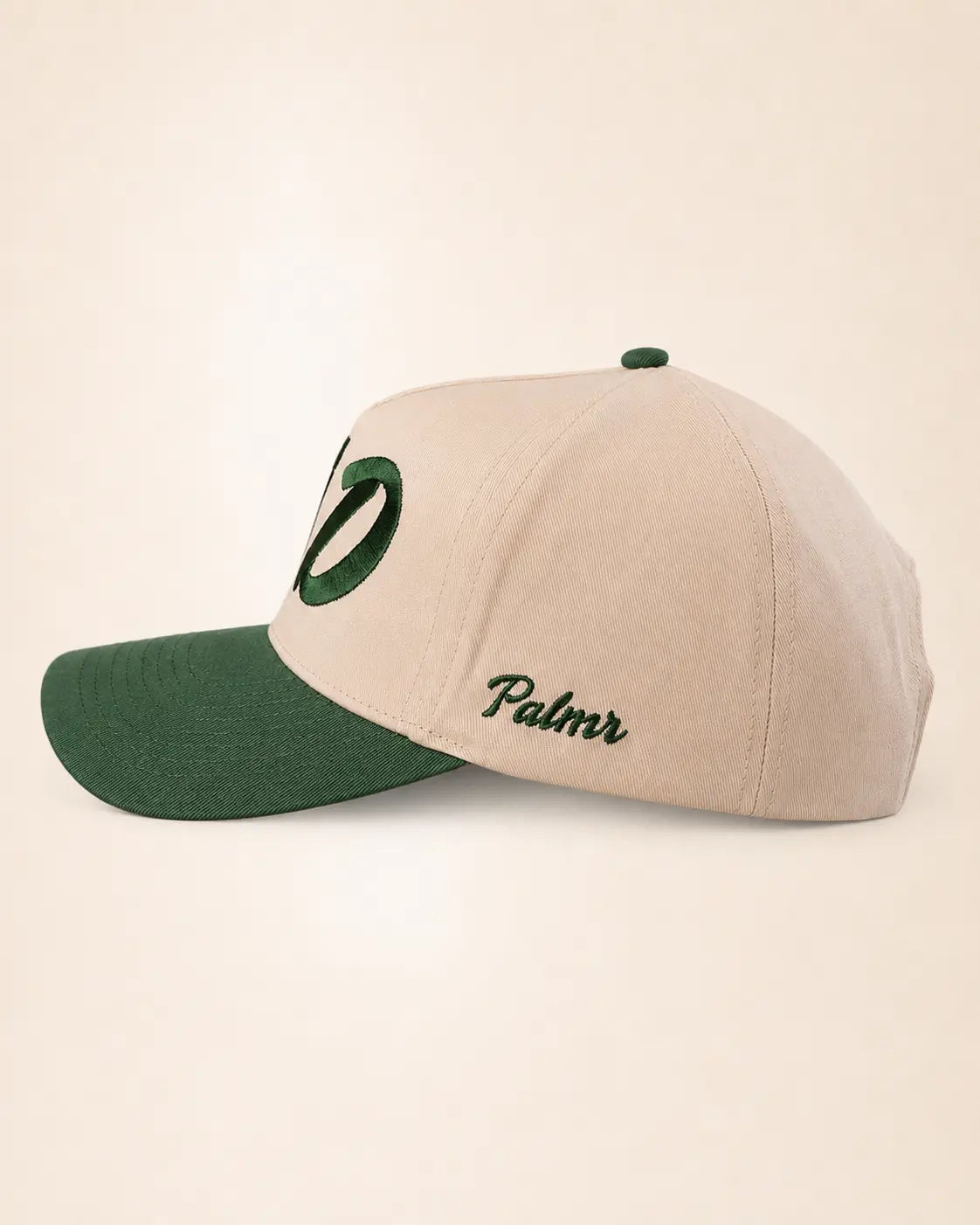 A structured baseball cap in beige and dark green, featuring a green embroidered oval logo on the front and the word 'Palmr' in green script on the side, set against a plain beige background.