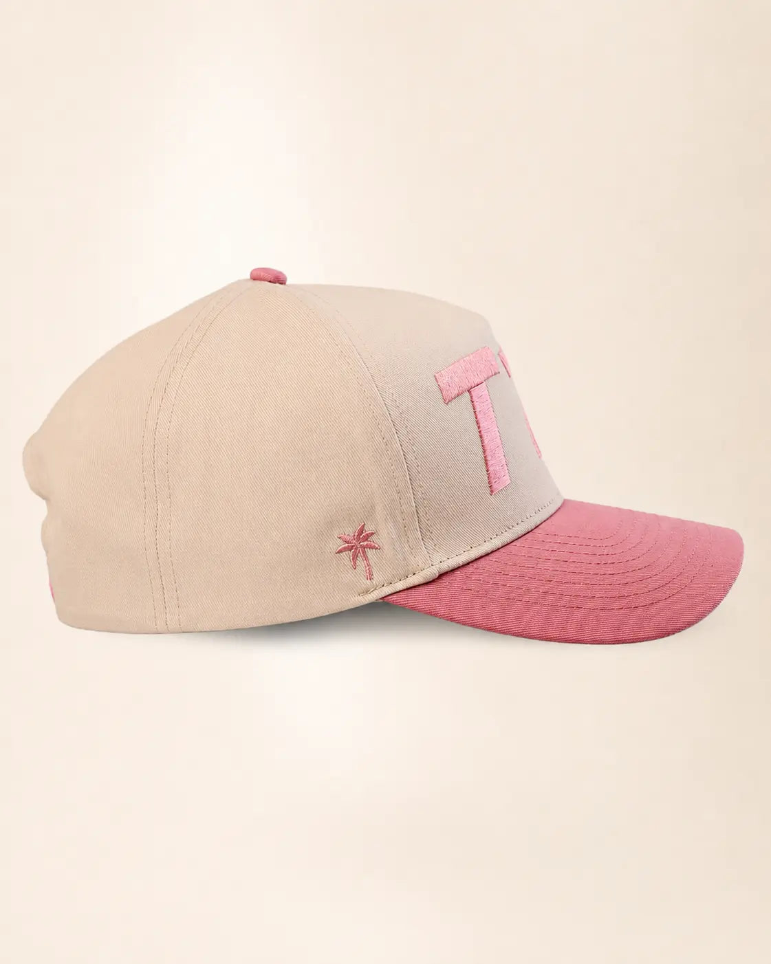 A baseball cap in beige and pink, featuring a large pink embroidered letter 'T1D' on the front and a small pink embroidered star on the side, set against a plain beige background.