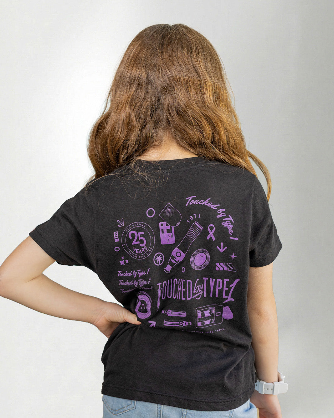 Girl wearing a black "touched by type 1" with purple diabetes related designs against a gray background.