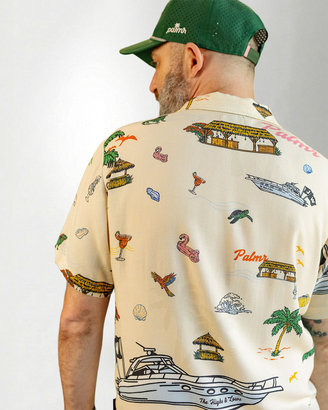 Man wearing a patterned shirt and striped shorts with a cap on a plain background