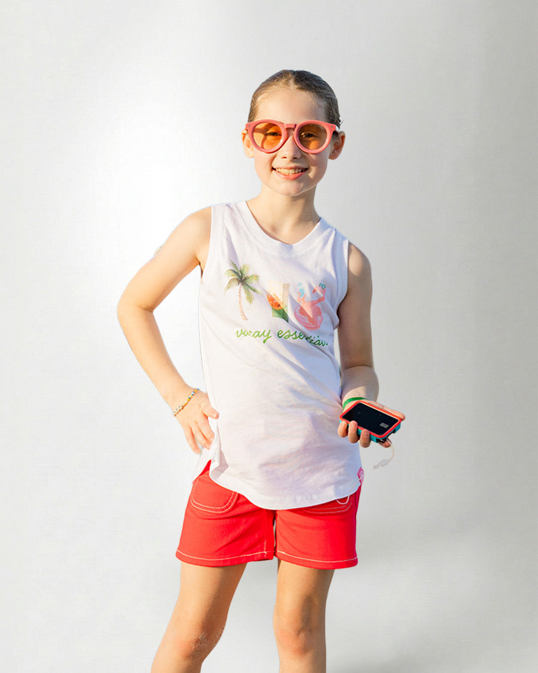Young girl wearing a white sleeveless shirt with graphics and text, standing against a plain background