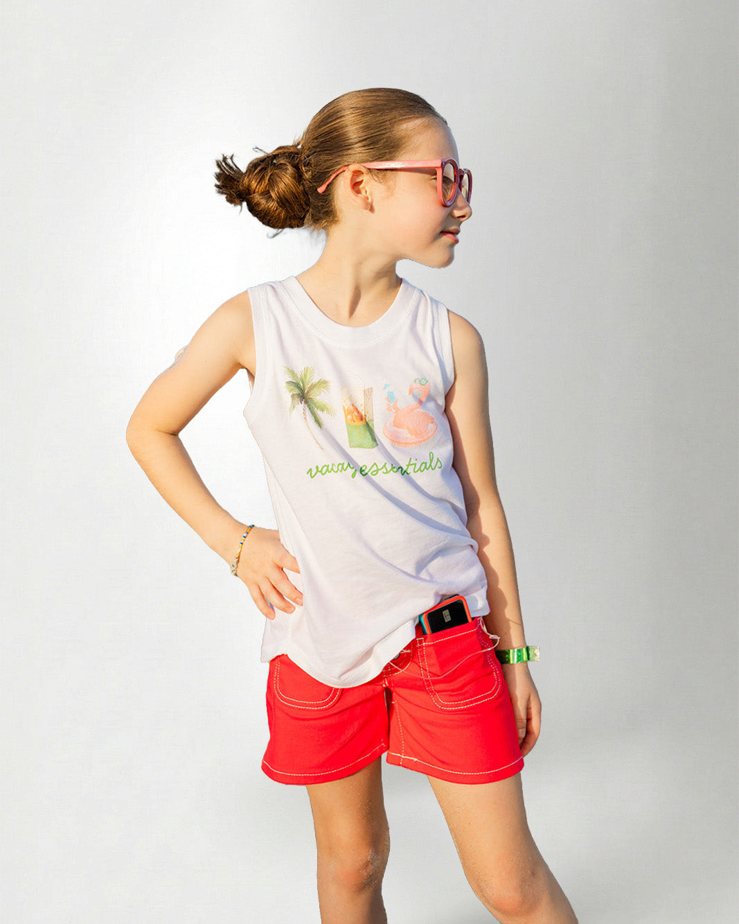 Young girl wearing a white sleeveless shirt with graphics and text, standing against a plain background