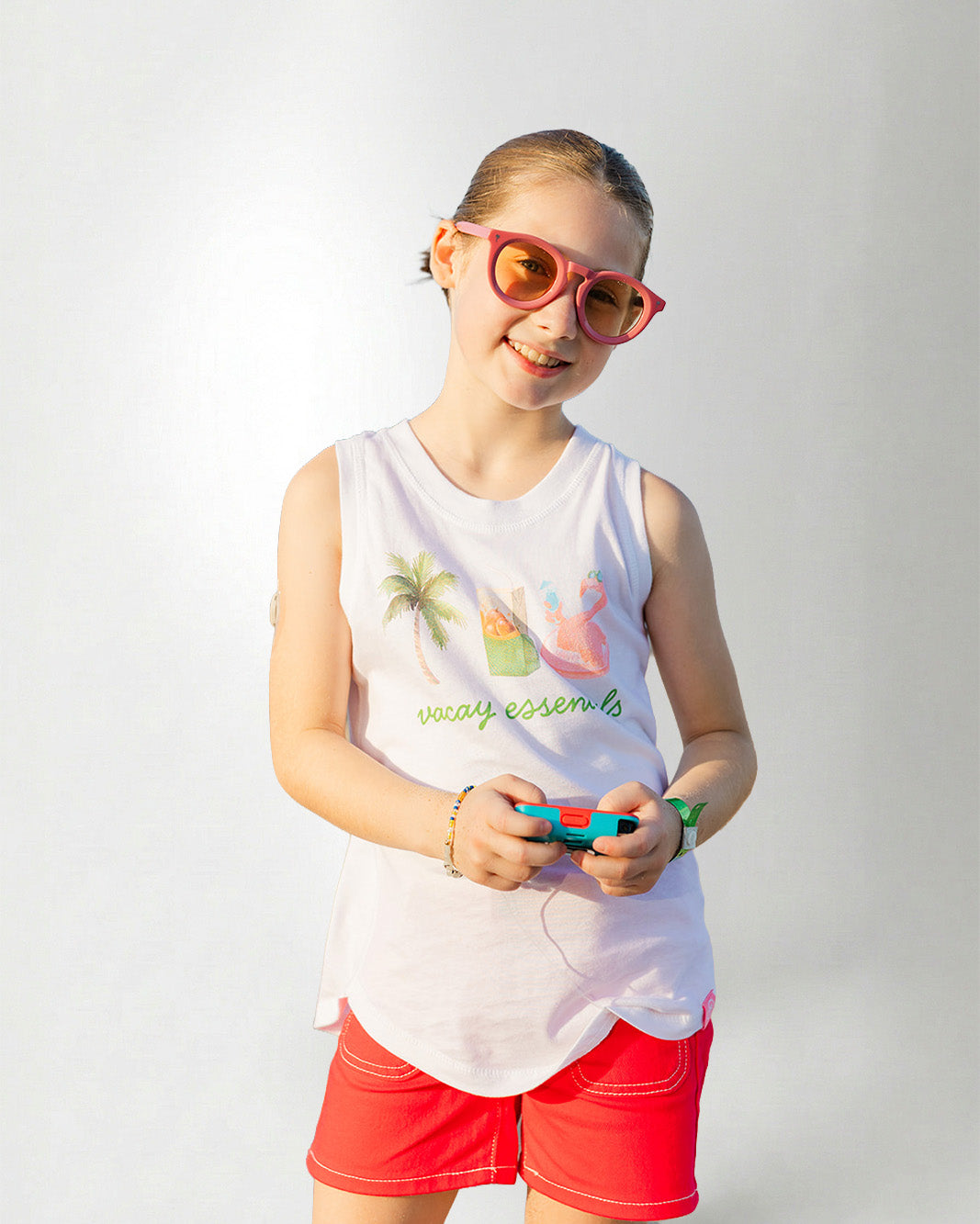 Young girl wearing a white sleeveless shirt with graphics and text, standing against a plain background