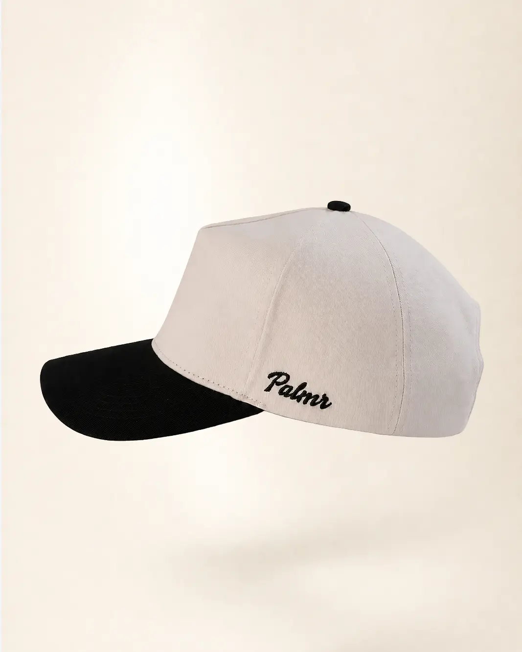 A baseball cap with a light beige crown and a black curved brim, featuring the name 'Palmier' embroidered in black script on the side, set against a solid cream background.