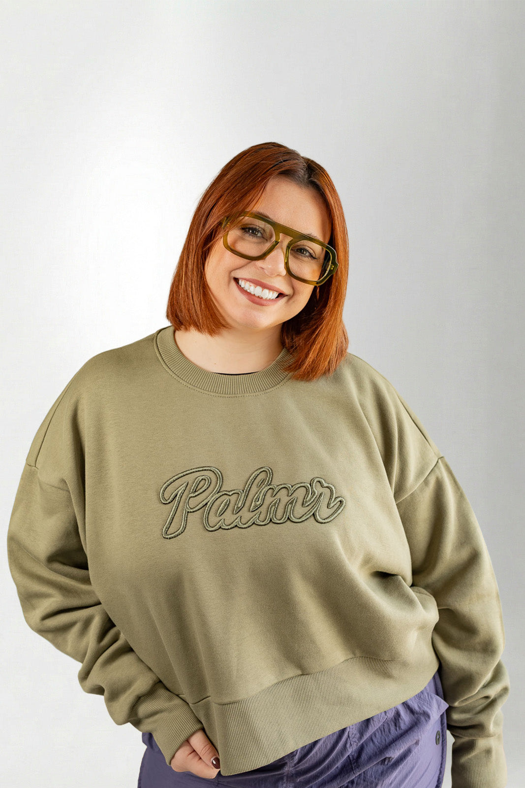 Person wearing a beige sweatshirt with 'Palmer' text on a plain background