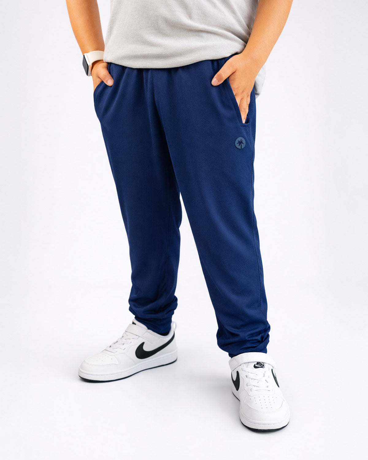Person wearing navy blue jogger pants and white sneakers on a white background
