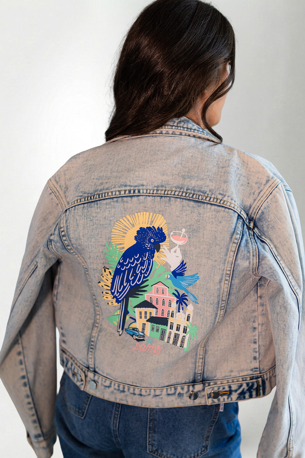 Denim jacket with a colorful parrot design on the back, worn by a person.