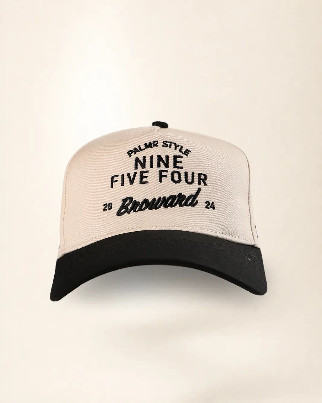 A baseball cap with a cream-colored crown and a black brim, featuring black embroidered text on the front that reads 'PALMR STYLE NINE FIVE FOUR Broward 2026'.