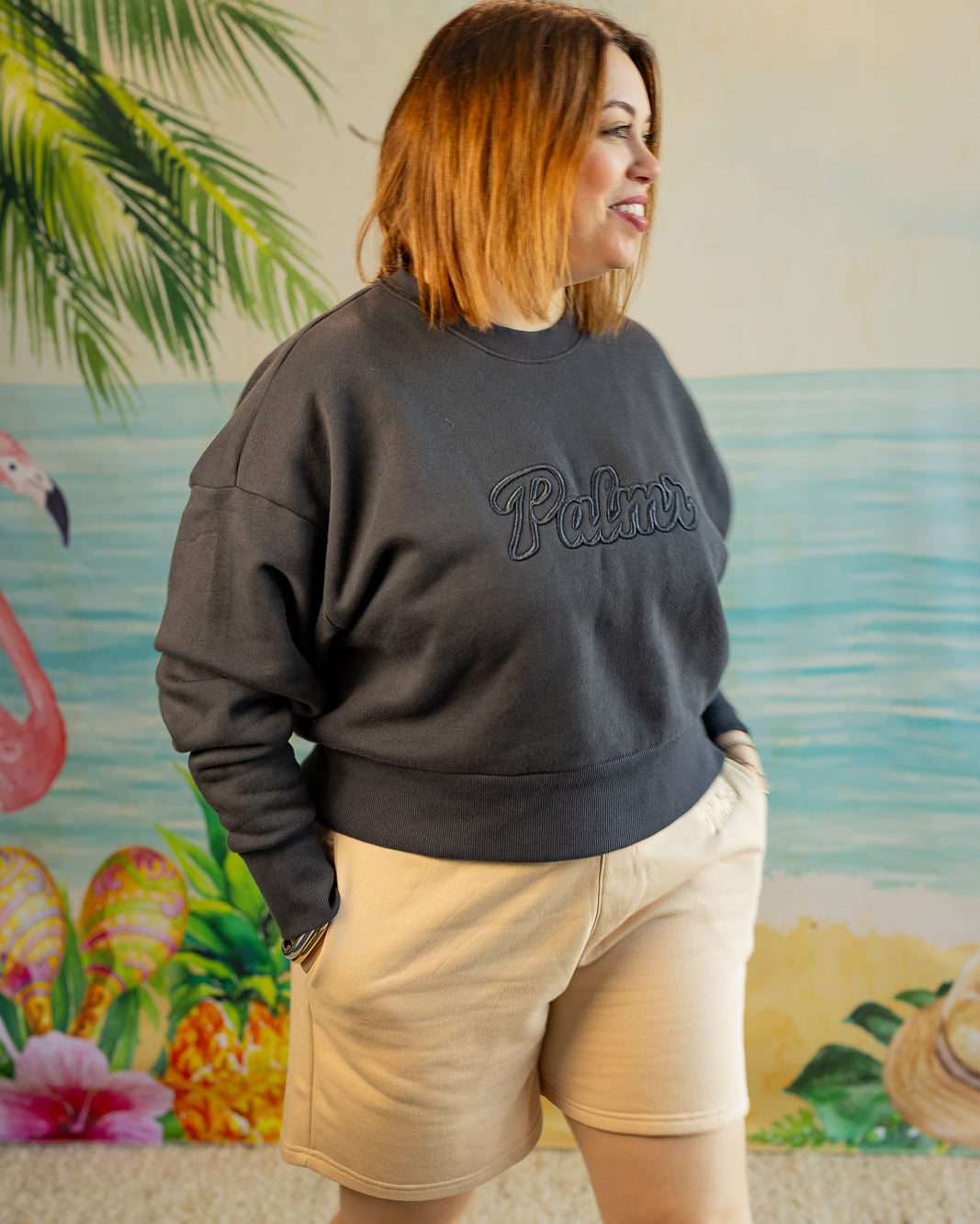 Person wearing a dark gray sweatshirt with 'Pullover' text, standing in front of a tropical-themed wall.
