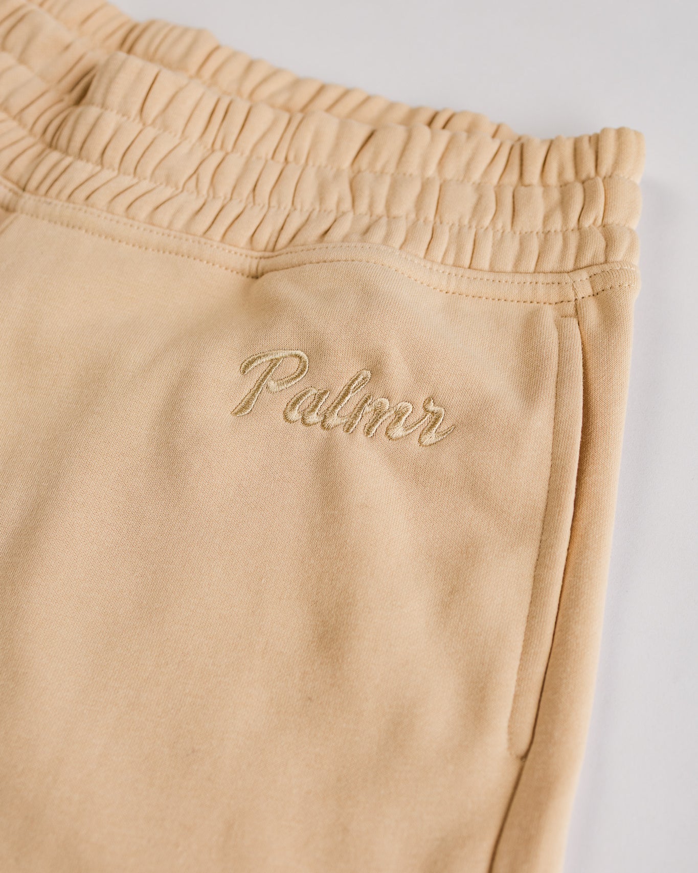 Beige sweatpants with 'Palmr' embroidery on a light gray background