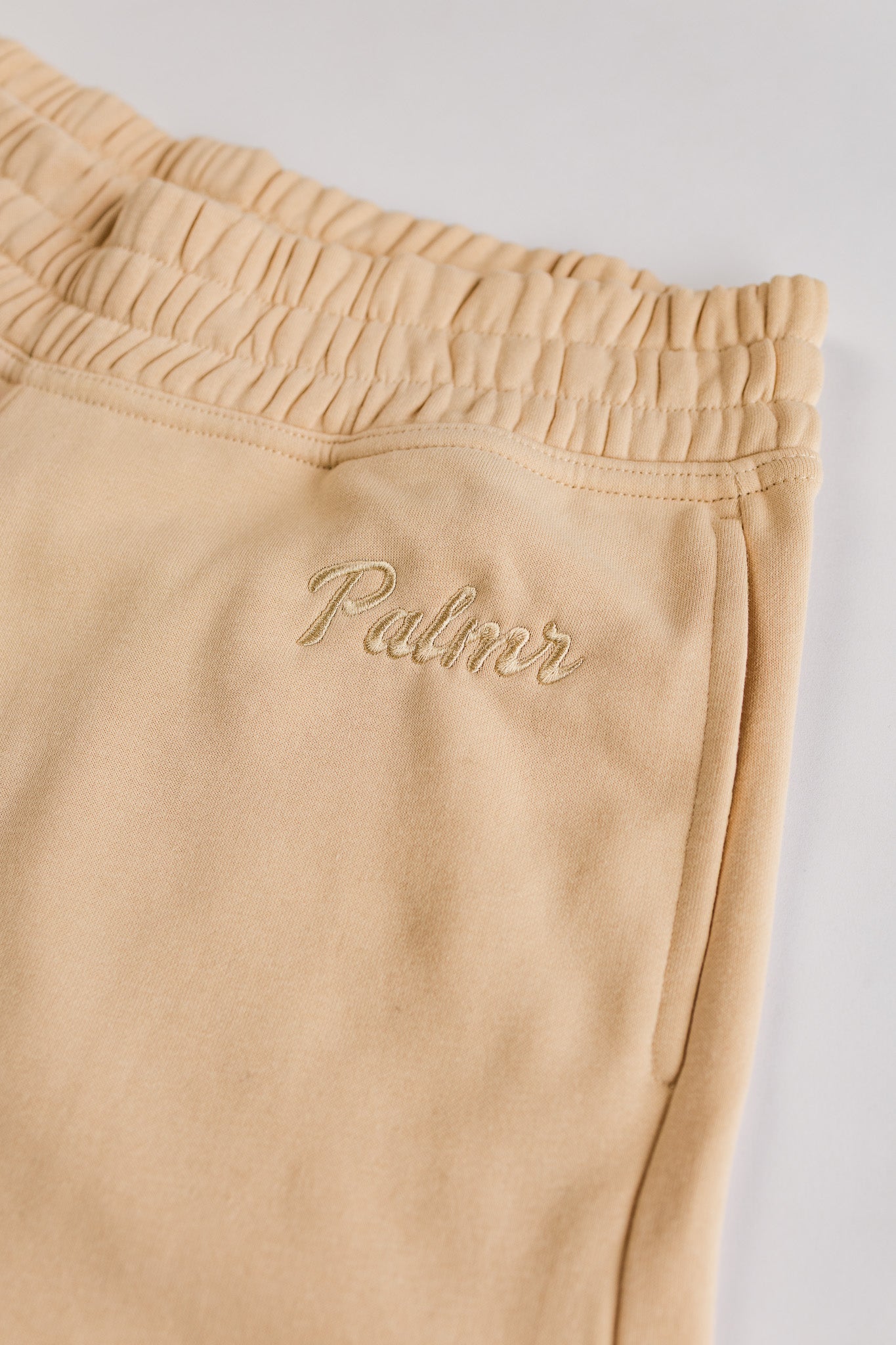 Beige sweatpants with 'Palmr' embroidery on a light gray background
