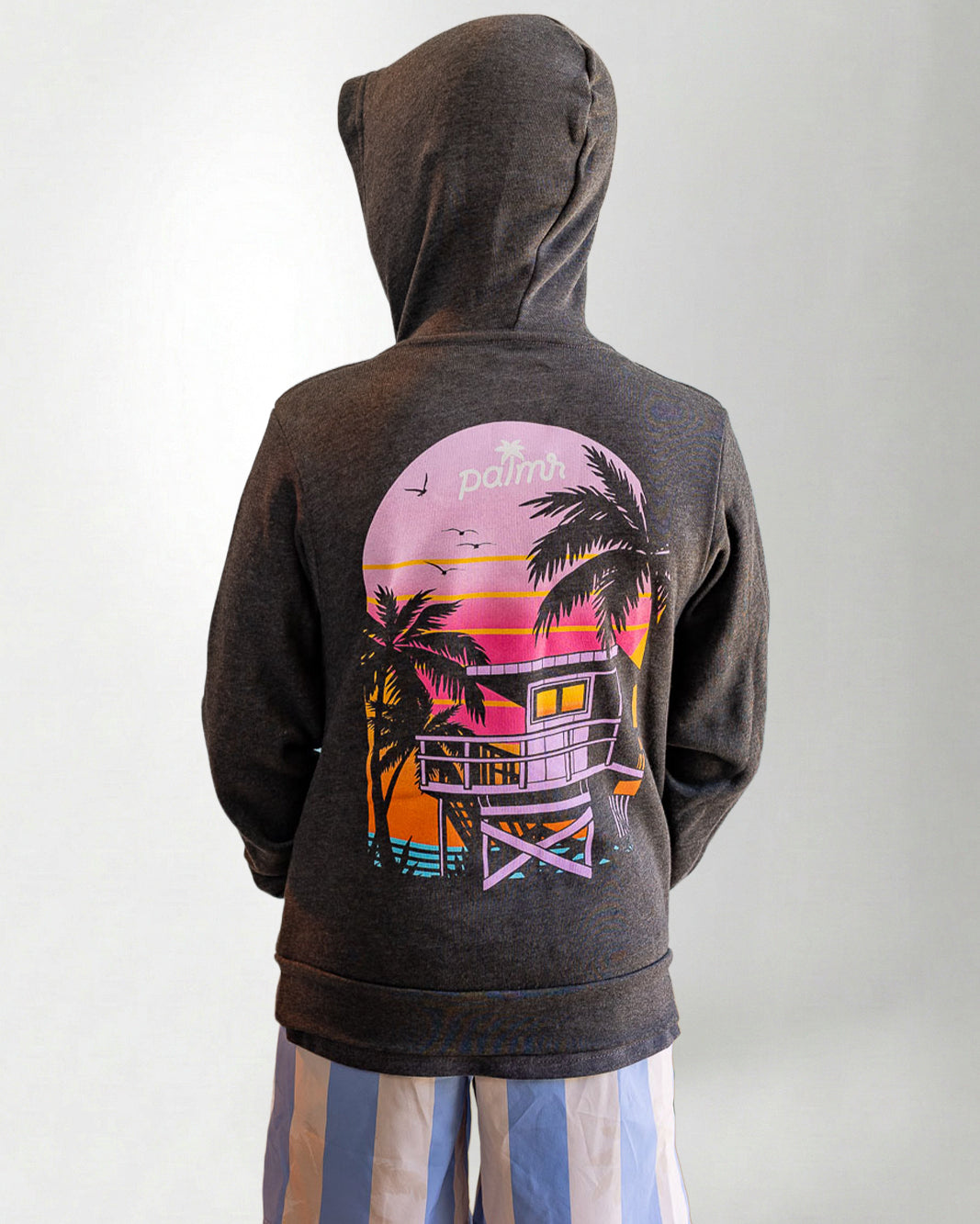 Person wearing a hoodie with a sunset and palm tree design on the back, standing against a plain background.