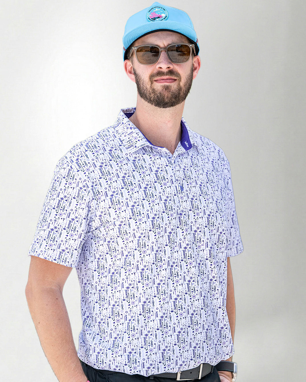 Man wearing a patterned shirt, sunglasses, and a blue cap against a plain background