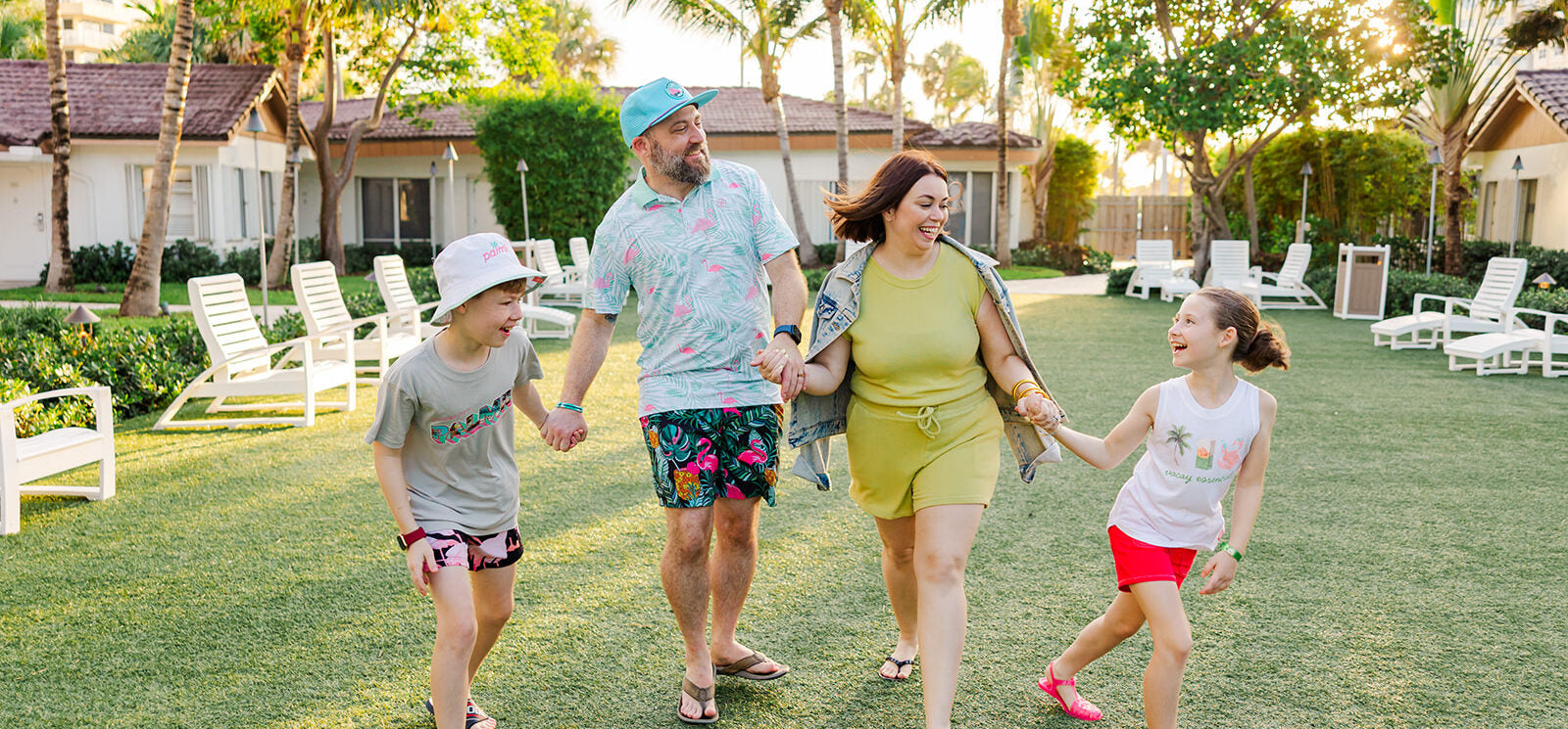 Nick, Rebecca and their two kids walking hand in hand across a lawn under palm trees, laughing