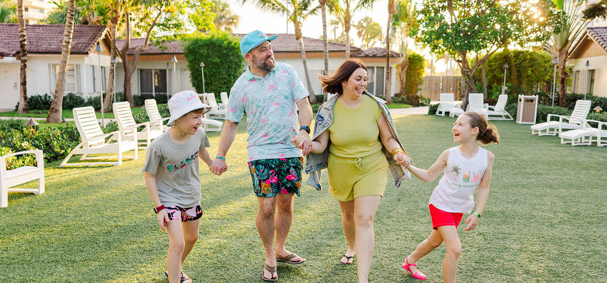 Nick, Rebecca and their two kids walking hand in hand across a lawn under palm trees, laughing