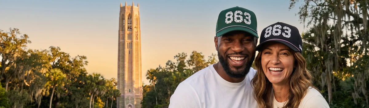 Couple in Palmr 863 Signature hats, green and black, with Bok Tower rising over the Lake Wales ridge behind them