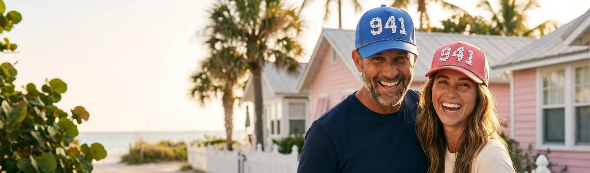 Couple in Palmr 941 Signature hats, blue and pink, in front of pastel beach cottages and palms in Sarasota
