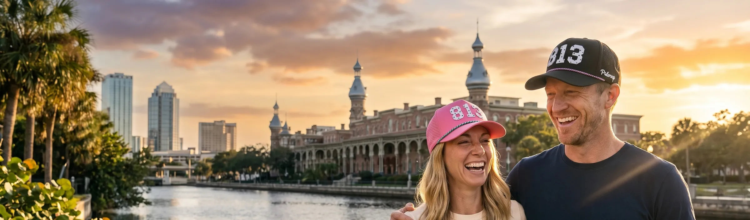 Couple wearing Palmr 813 Signature hats on the Tampa Riverwalk with the University of Tampa minarets across the Hillsborough River