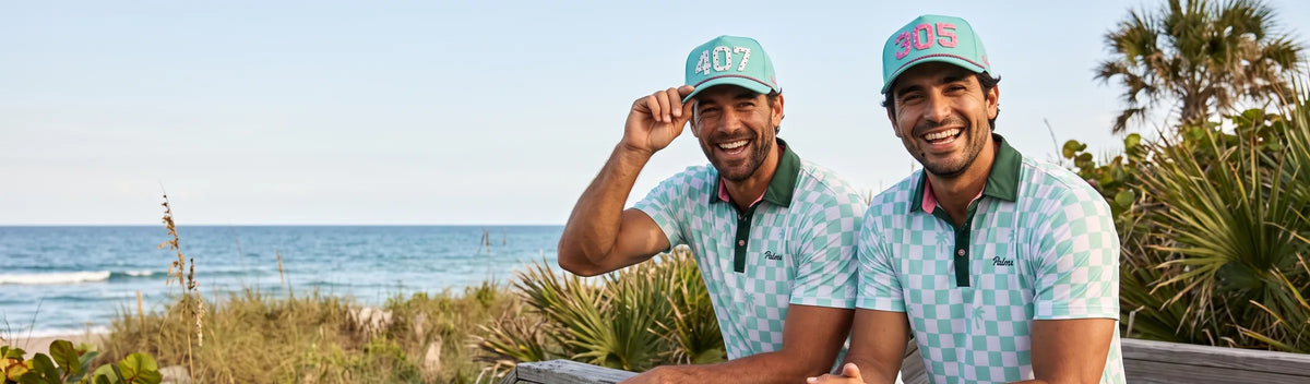 Two friends on a Florida beach boardwalk in Palm Court checkerboard polos, one in the 407 Signature hat in teal and one in the 305 Signature hat in pink on teal