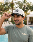 A man wearing the cream and black 813 Tampa Bay Heritage Hat and a gray t-shirt with 'Palmr' embroidered on the chest, posing by a pool with a blurred background.