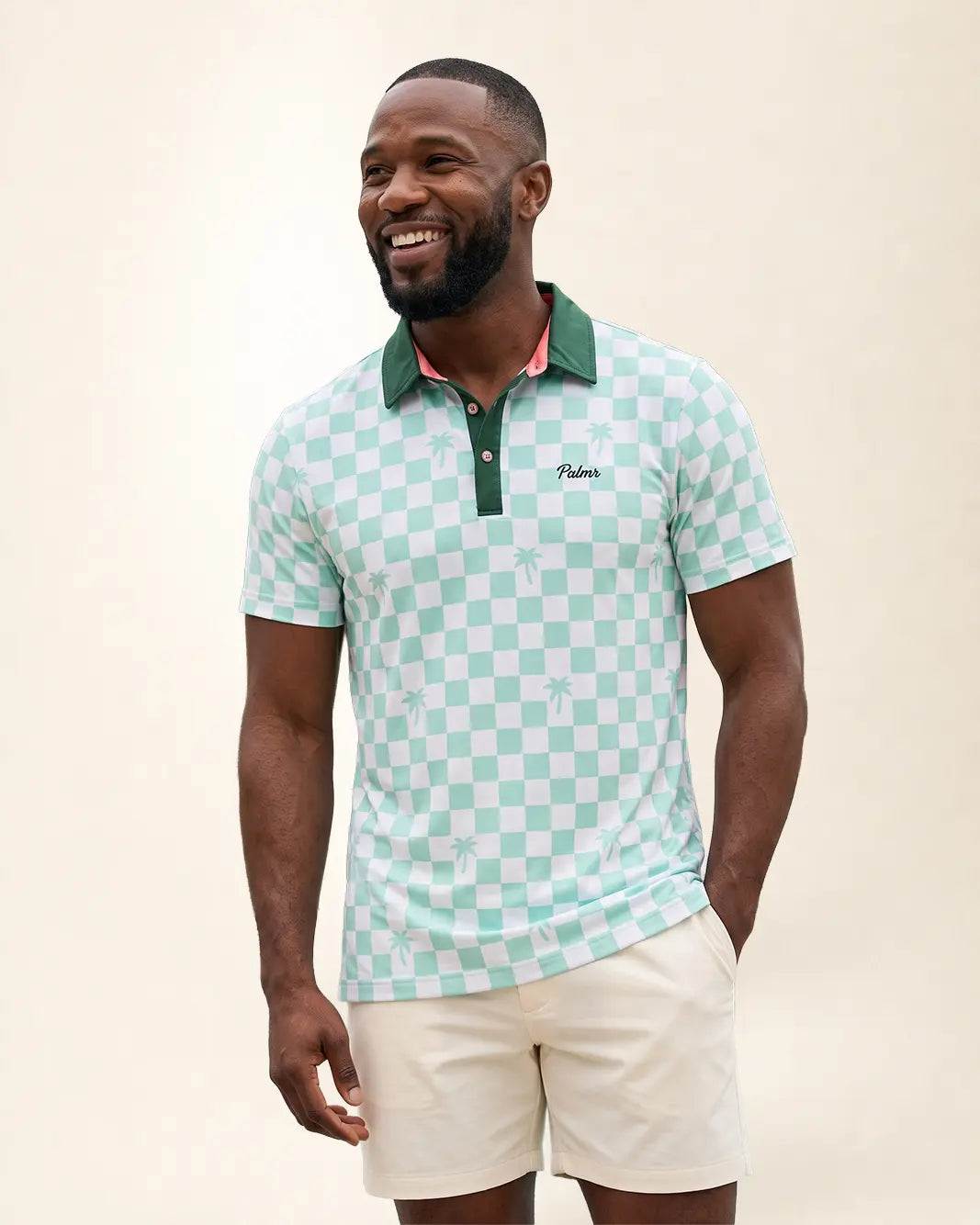 A man wearing a mint green and white checkered polo shirt with a green collar and white shorts, standing against a light beige background.