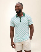 A man wearing a mint green and white checkered polo shirt with a green collar and white shorts, standing against a light beige background.