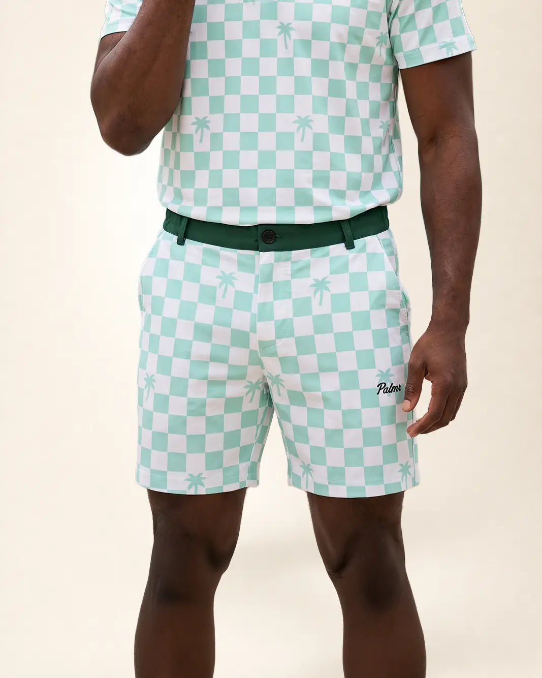 A man wearing a mint green and white checkered short-sleeve polo shirt and matching shorts with a dark green belt. The shorts feature a small embroidered 'Palmr' logo on the lower left leg.